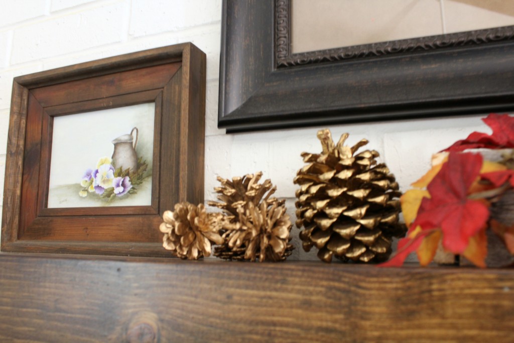 gold-pine-cones-and-small-painting-on-mantel